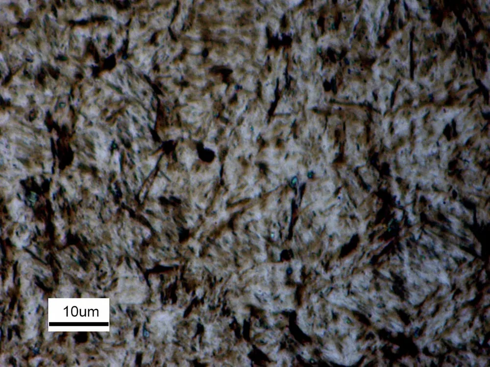 Micrografia óptica de martensita em aço AISI 4140, com aspecto acicular e barra de escala de 10 micrometros.