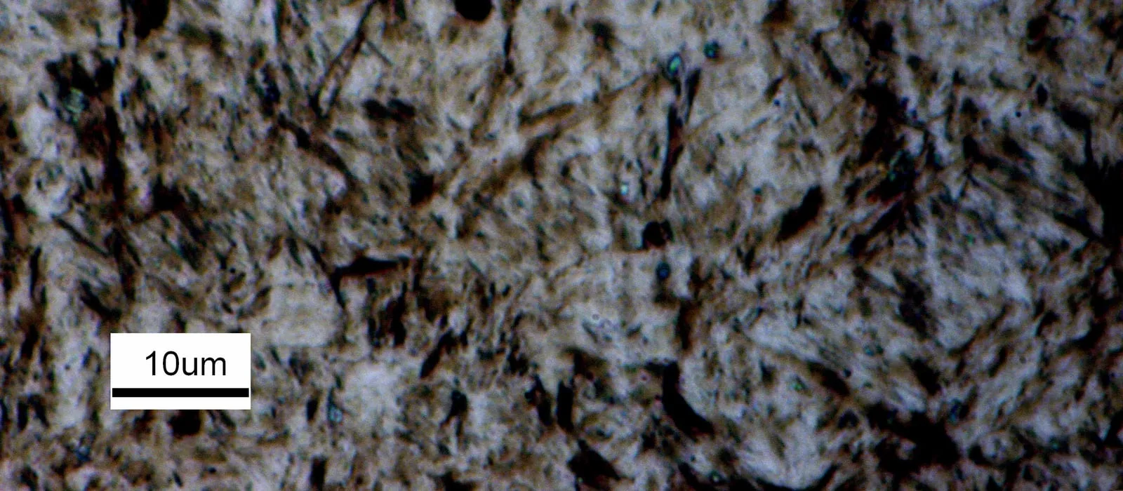 Micrografia óptica de martensita em aço AISI 4140 temperado em óleo, com barra de escala de 10 micrometros.